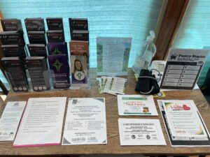 A table is pictured with a collection of fact sheets, handouts, and pamphlets. They cover topics like healthy eating and other places you can get support with food and health.