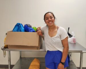 A woman leaning against a box of colorful drawstring bags. 